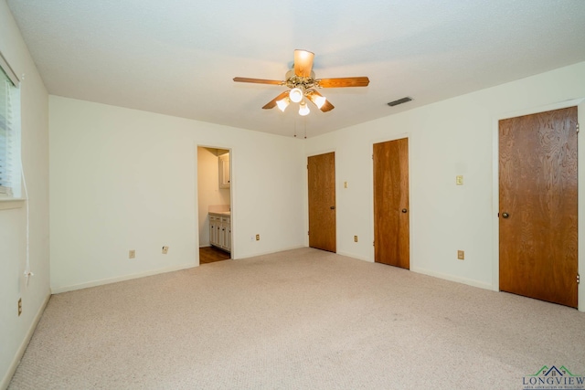 unfurnished bedroom with ensuite bath, ceiling fan, light carpet, and two closets