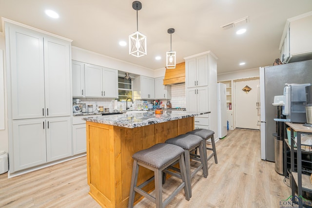 kitchen featuring light wood finished floors, freestanding refrigerator, a breakfast bar area, and a center island