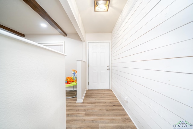 hallway featuring wood walls, beamed ceiling, and light hardwood / wood-style floors