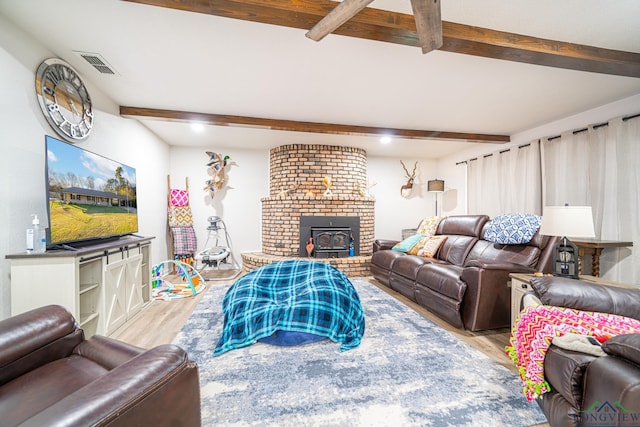 living room featuring a wood stove, beamed ceiling, and light hardwood / wood-style floors