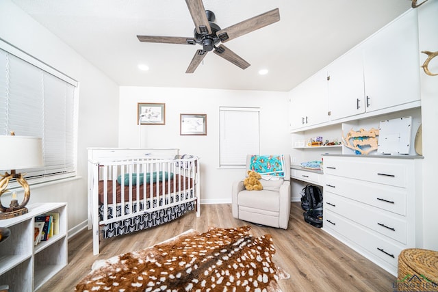 bedroom with light wood-type flooring, a nursery area, and ceiling fan