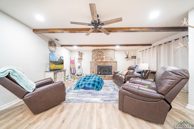 living room with light hardwood / wood-style floors, ceiling fan, beam ceiling, and a wood stove