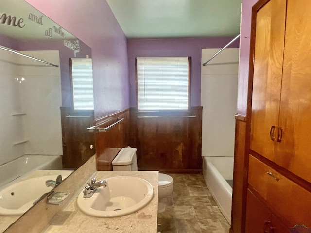 full bathroom with wood walls, toilet,  shower combination, and sink