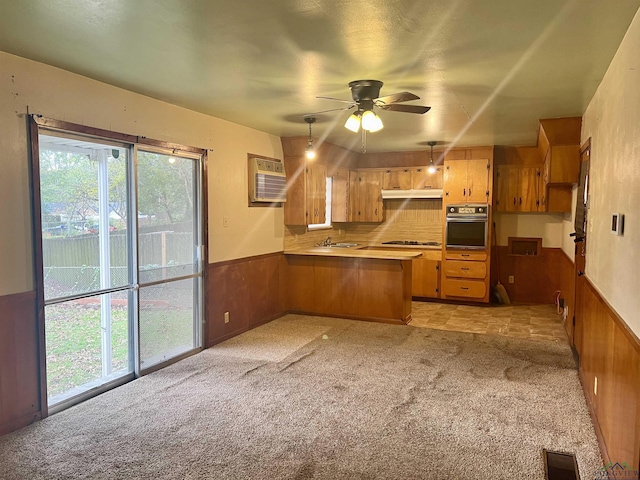 kitchen featuring kitchen peninsula, light carpet, ceiling fan, wooden walls, and oven