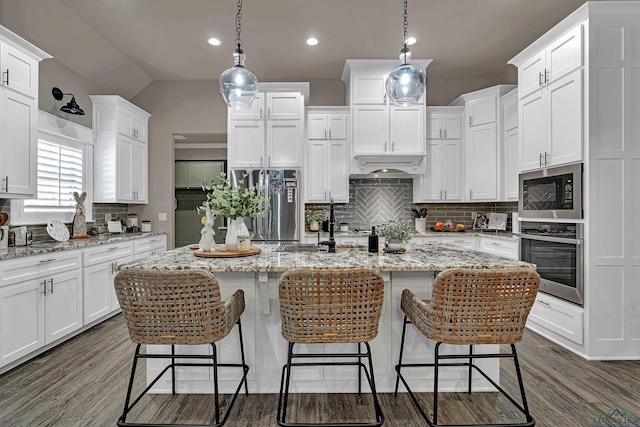 kitchen with appliances with stainless steel finishes, hanging light fixtures, white cabinets, and a center island with sink