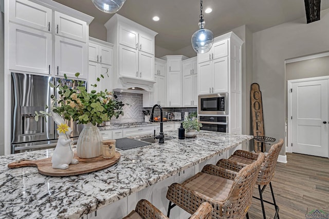 kitchen with appliances with stainless steel finishes, a breakfast bar, light stone counters, white cabinetry, and pendant lighting