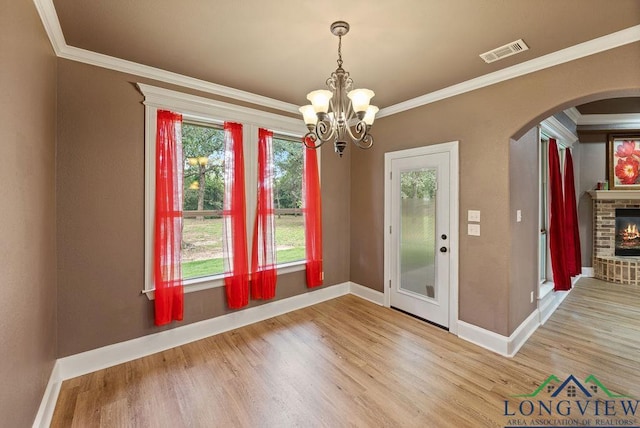 unfurnished dining area with a fireplace, hardwood / wood-style flooring, crown molding, and a notable chandelier