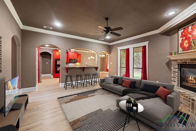 living room with a fireplace, light hardwood / wood-style floors, ceiling fan with notable chandelier, and ornamental molding