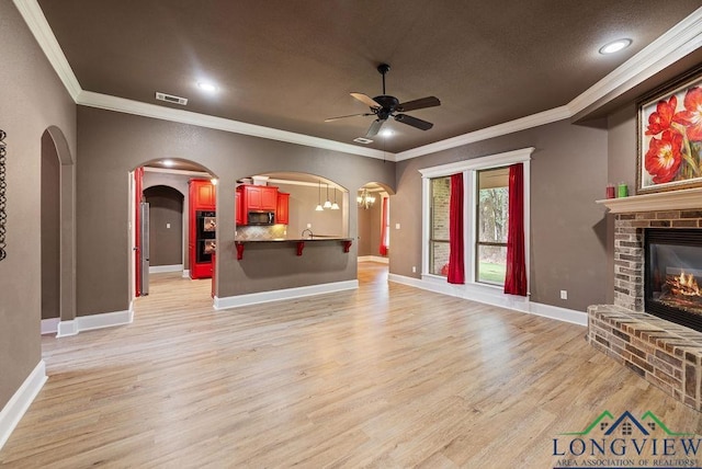 unfurnished living room featuring crown molding, ceiling fan, light wood-type flooring, and a brick fireplace