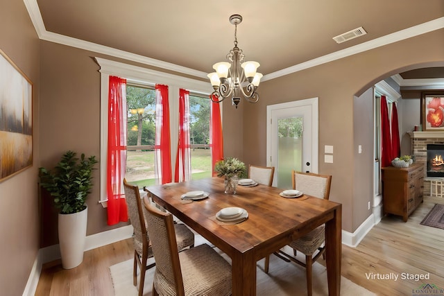 dining room with a notable chandelier, a stone fireplace, crown molding, and light hardwood / wood-style flooring