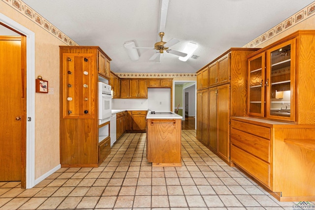 1208 Marigold Ln, Longview, TX 75604 - kitchen with brown cabinetry, a ceiling fan, glass insert cabinets, light countertops, and cooktop