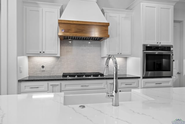 113 Saddle Brook Cir, Hallsville, TX 75650 - kitchen with custom range hood, stainless steel oven, cooktop, and white cabinetry