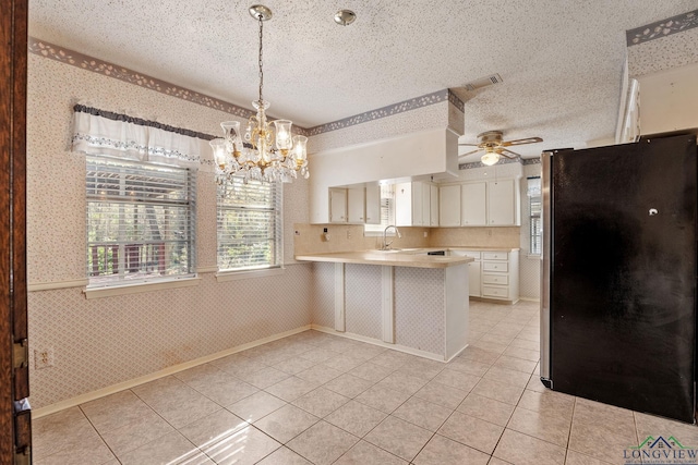 kitchen with white cabinets, black refrigerator, sink, decorative light fixtures, and kitchen peninsula