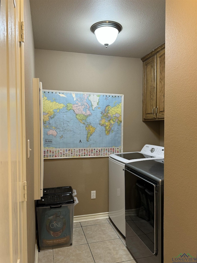 laundry area with washer and clothes dryer, light tile patterned flooring, cabinets, and a textured ceiling