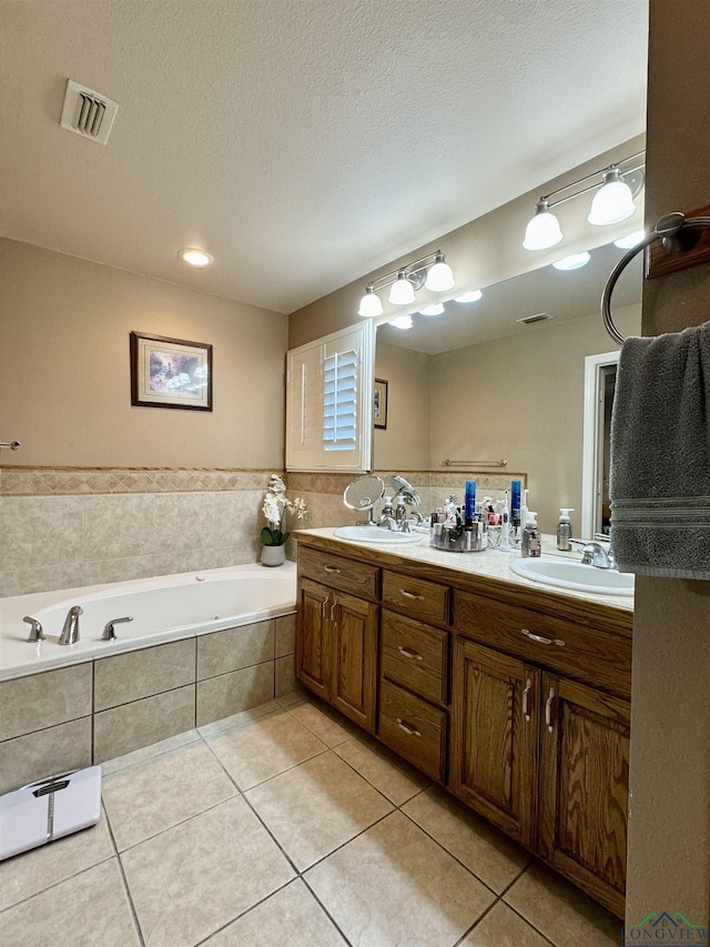 bathroom featuring a textured ceiling, vanity, a relaxing tiled tub, and tile patterned floors