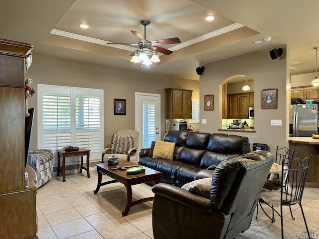 tiled living room with a raised ceiling, ceiling fan, and ornamental molding