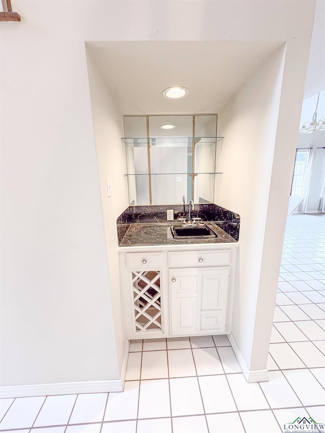 bar featuring light tile patterned floors, baseboards, indoor wet bar, and a sink