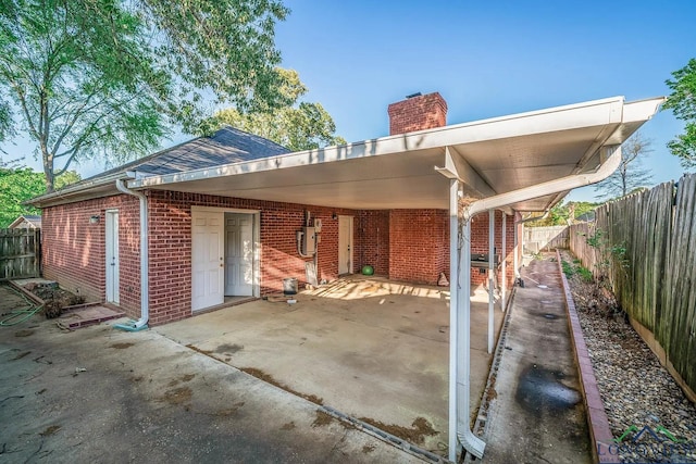 back of property with a patio, an attached carport, brick siding, a fenced backyard, and a chimney