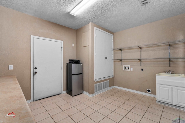 laundry room featuring electric dryer hookup, sink, washer hookup, light tile patterned floors, and a textured ceiling