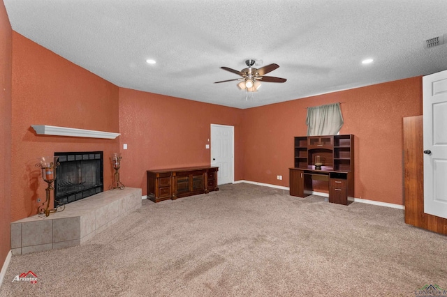 carpeted living room featuring a tiled fireplace, ceiling fan, and a textured ceiling