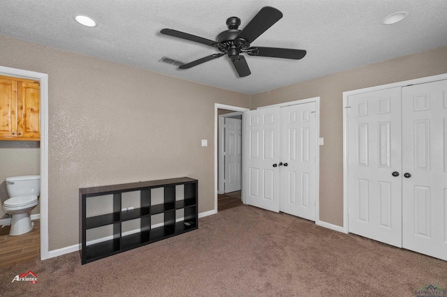 bedroom with dark colored carpet, ceiling fan, two closets, and ensuite bath