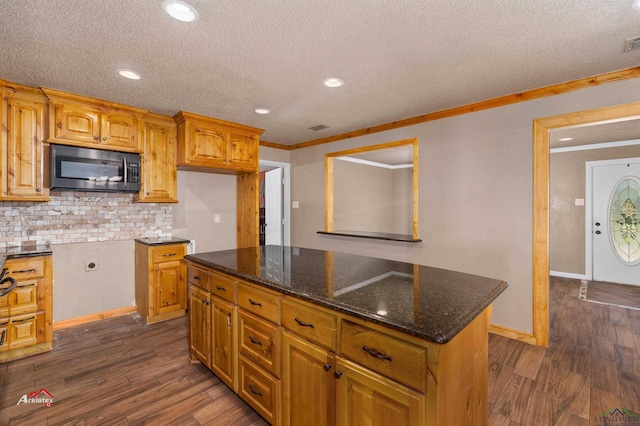 kitchen featuring crown molding, a center island, dark stone counters, and dark hardwood / wood-style floors