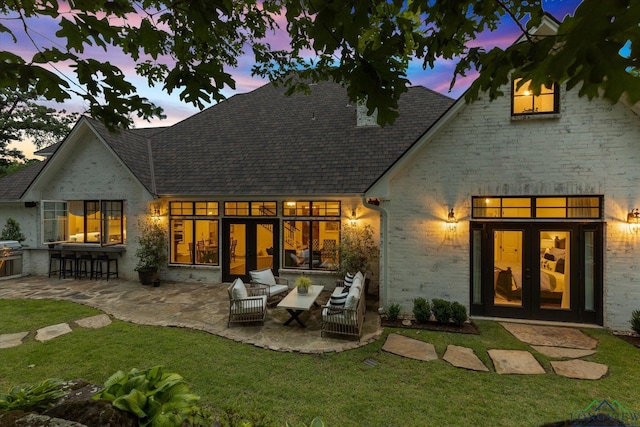 1307 Yates Dr, Longview, TX 75601 - back of house at dusk with french doors, a patio, brick siding, and a yard