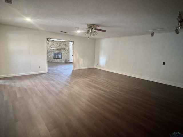 unfurnished living room featuring a textured ceiling, dark hardwood / wood-style flooring, a brick fireplace, and ceiling fan