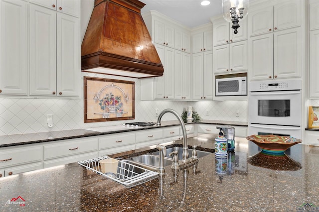 kitchen featuring white appliances, white cabinetry, dark stone counters, and custom exhaust hood