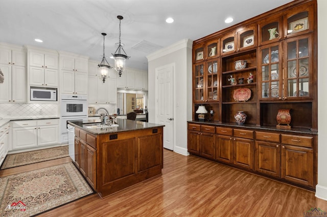 kitchen with white appliances, sink, pendant lighting, light hardwood / wood-style floors, and a kitchen island with sink