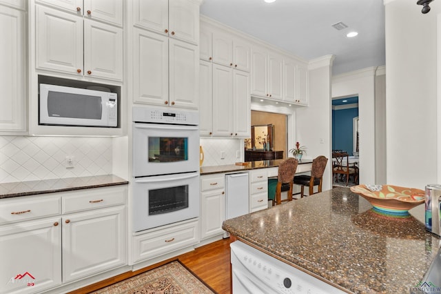 kitchen with white appliances, white cabinetry, dark stone counters, light hardwood / wood-style floors, and crown molding