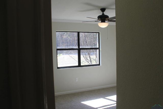 carpeted empty room with crown molding, a ceiling fan, and baseboards