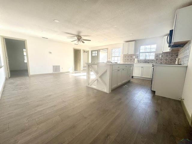 kitchen with backsplash, sink, wood-type flooring, a center island, and white cabinetry