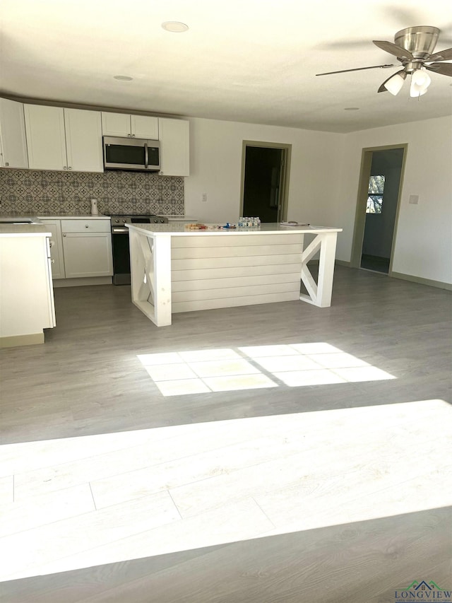 kitchen featuring light wood-type flooring, backsplash, stainless steel appliances, ceiling fan, and white cabinetry