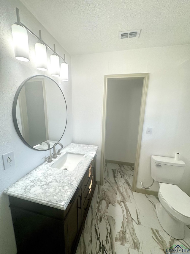 bathroom with vanity, toilet, and a textured ceiling