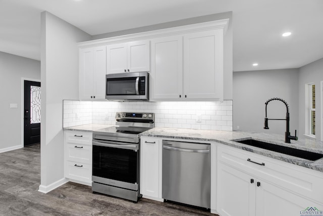 kitchen with appliances with stainless steel finishes, dark wood-type flooring, a sink, and light stone countertops