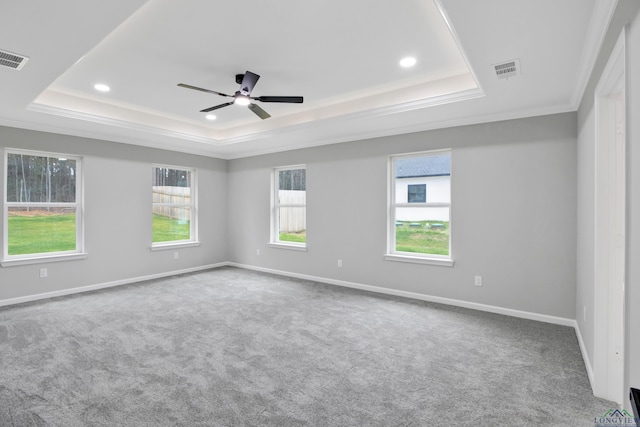 carpeted empty room featuring a raised ceiling, visible vents, ornamental molding, a ceiling fan, and baseboards