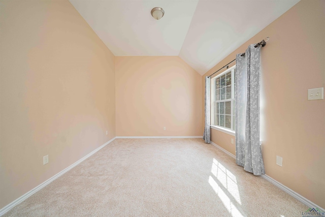 carpeted spare room featuring vaulted ceiling and baseboards