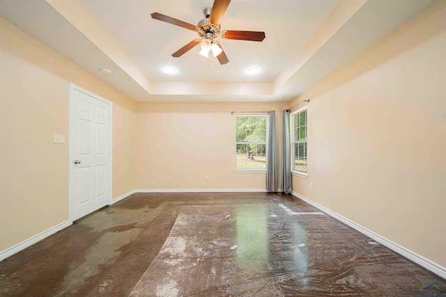 empty room featuring concrete floors, ceiling fan, baseboards, and a tray ceiling