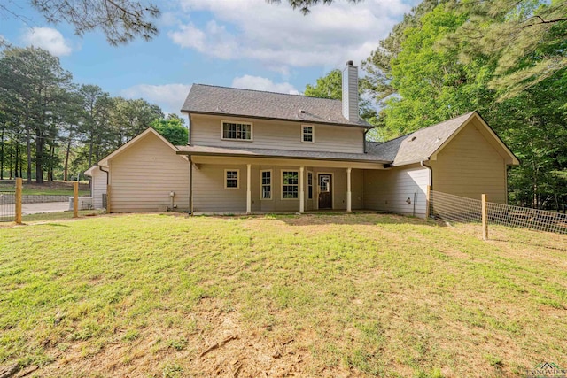 back of house featuring a chimney, fence, and a lawn