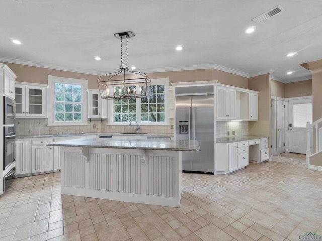 kitchen with sink, hanging light fixtures, a kitchen island, built in appliances, and white cabinets