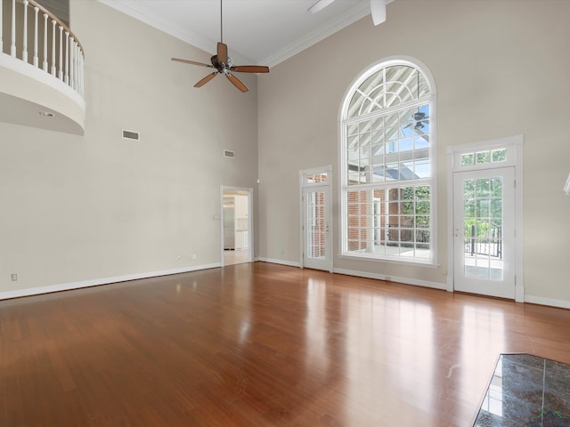 unfurnished living room featuring wood-type flooring, a towering ceiling, ceiling fan, and ornamental molding