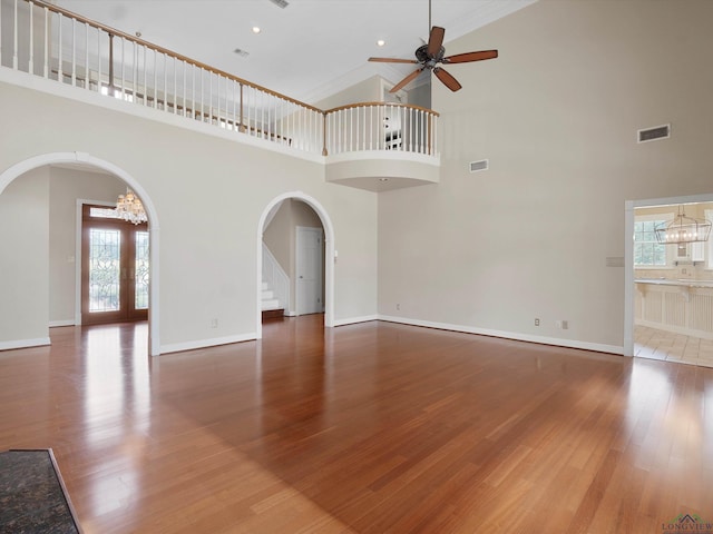 unfurnished living room with a high ceiling, french doors, ceiling fan with notable chandelier, ornamental molding, and wood-type flooring