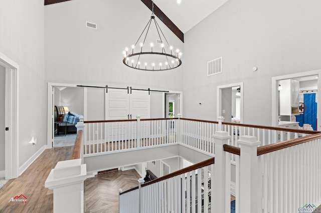 staircase with beam ceiling, parquet floors, a barn door, high vaulted ceiling, and a notable chandelier