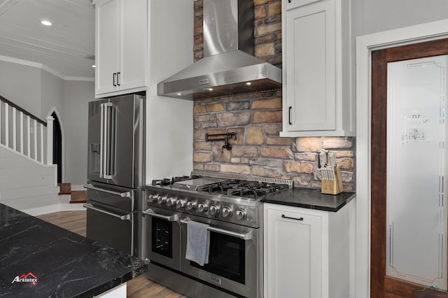 kitchen with high quality appliances, wall chimney range hood, crown molding, hardwood / wood-style flooring, and white cabinetry