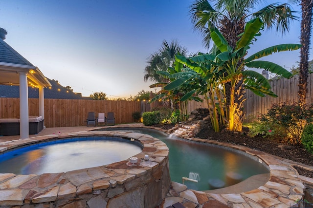 pool at dusk featuring an in ground hot tub