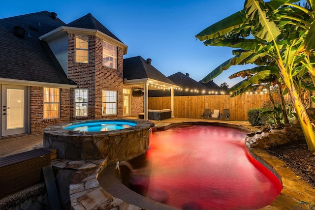 pool at dusk with an in ground hot tub