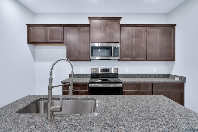 kitchen with appliances with stainless steel finishes, dark stone counters, and sink