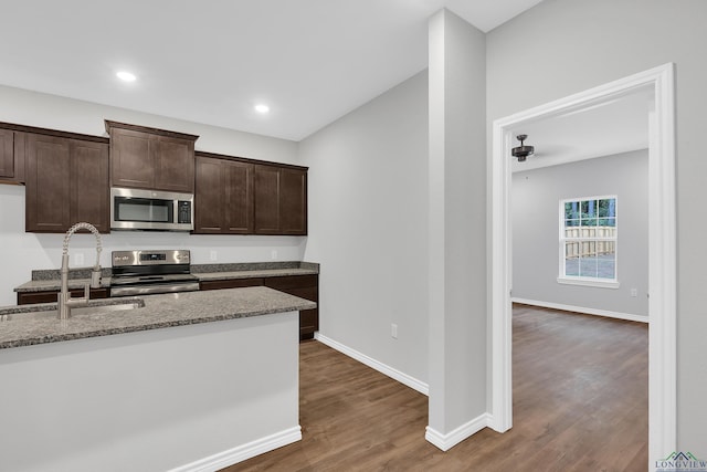 kitchen featuring light stone countertops, sink, dark hardwood / wood-style floors, dark brown cabinets, and appliances with stainless steel finishes