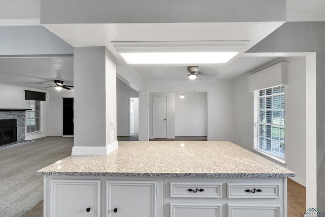 kitchen featuring ceiling fan, light stone counters, a fireplace with raised hearth, white cabinetry, and open floor plan